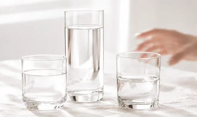 Tri poháre čerstvej vody v rôznych veľkostiach na svetlom stole